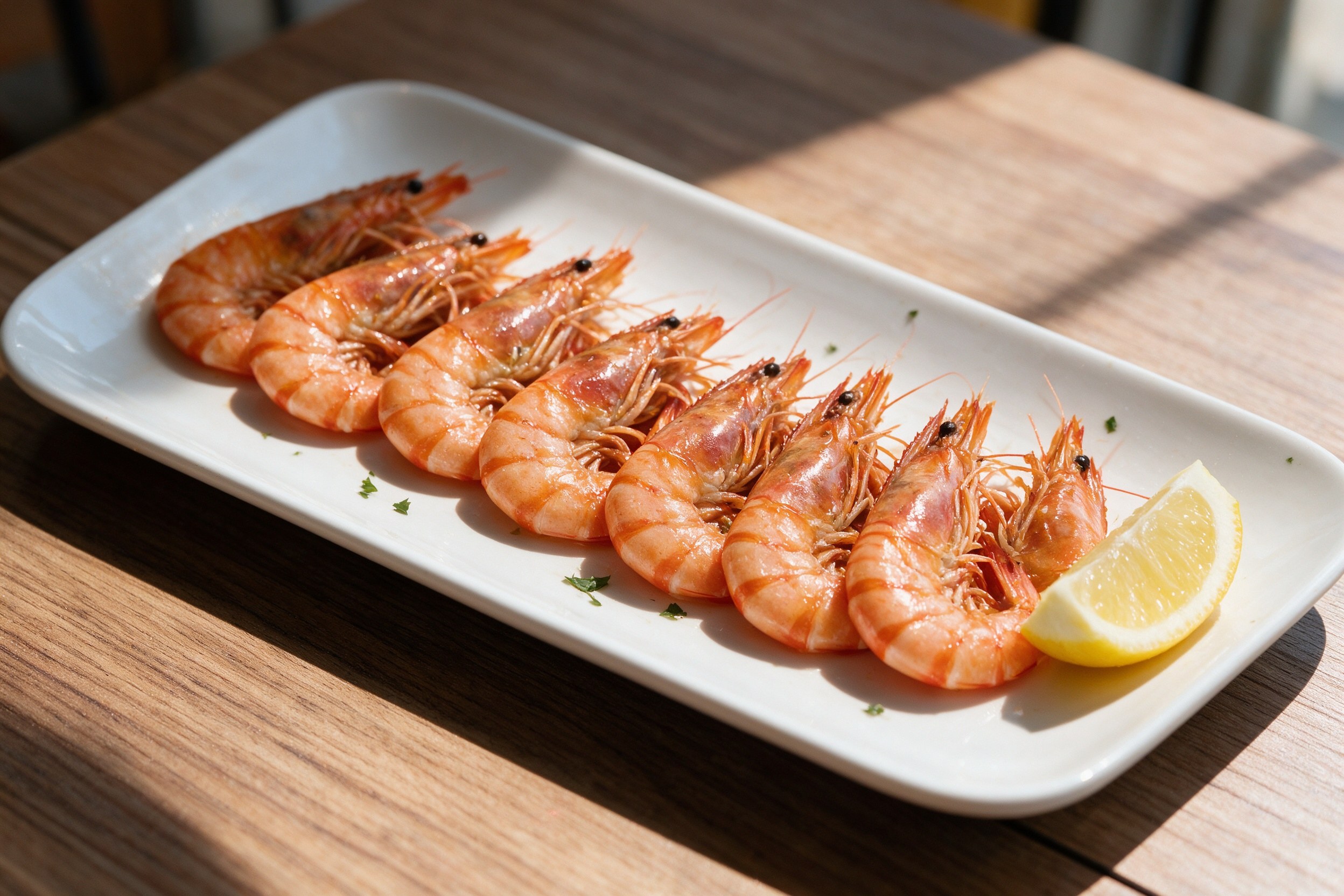 Langostinos cocidos en plato blanco alargado con gajo de limón